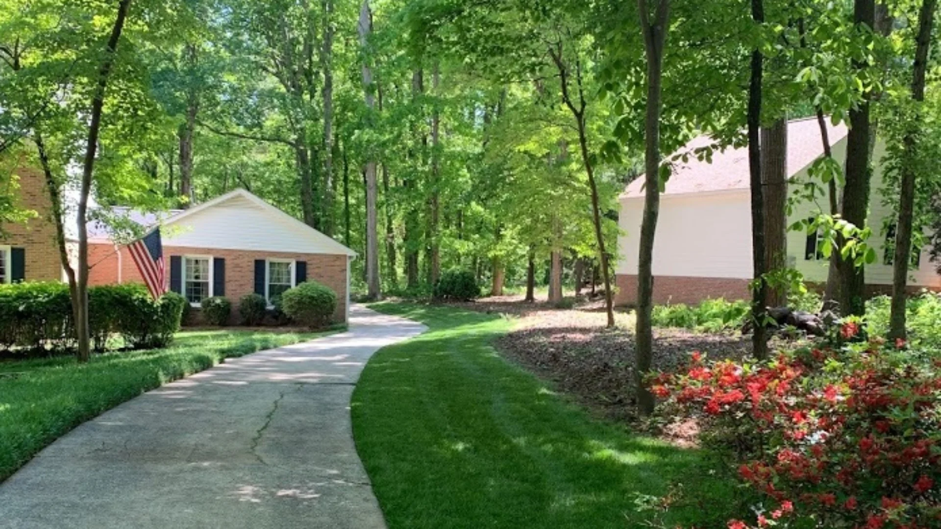 House in Charlotte, NC surrounded by trees, lawn, shrubs, and flowers.