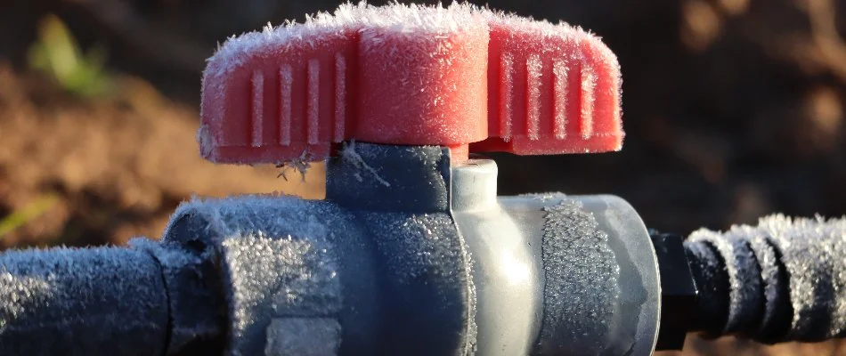 An irrigation system in Charlotte, NC, with a red handle and black pipe covered in ice.