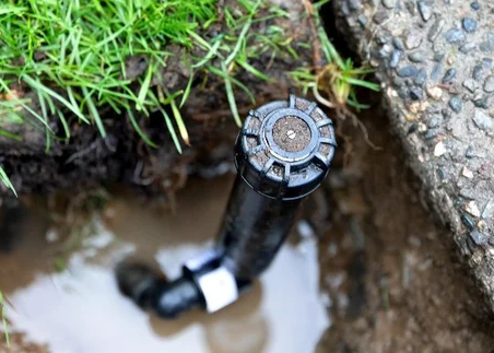 Broken sprinkler head in muddy ground, illustrating irrigation issues that waste water and money, relevant to FineTurf's irrigation services.