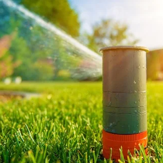 Irrigation sprinkler head spraying water on lush green lawn, illustrating effective irrigation system maintenance for healthy landscapes.
