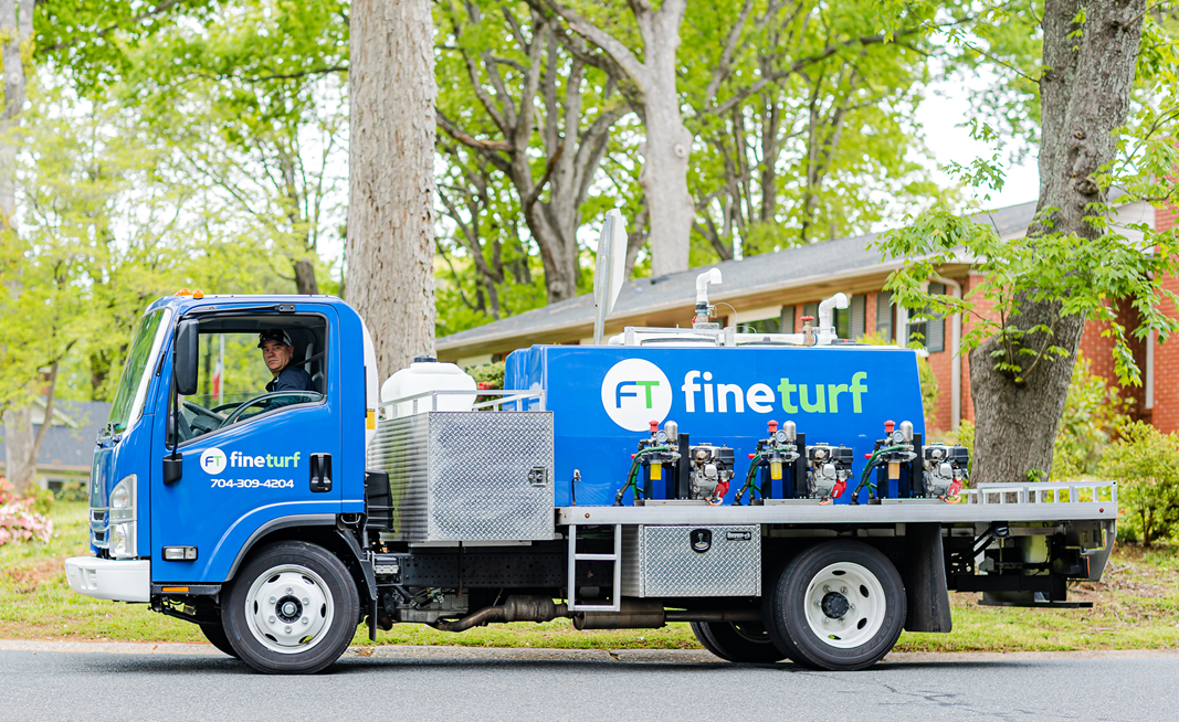 Blue FineTurf truck with logo and equipment for lawn care services parked in residential area, emphasizing local expertise in Charlotte.