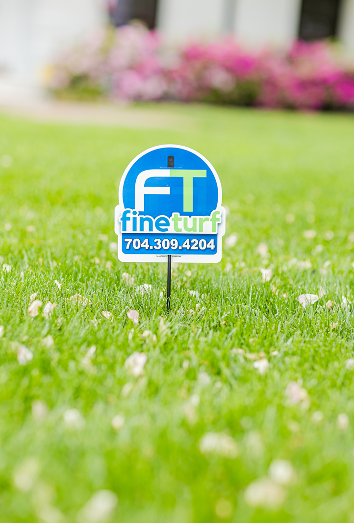 FineTurf lawn care sign in lush green grass, promoting topdressing services with contact number 704.309.4204.