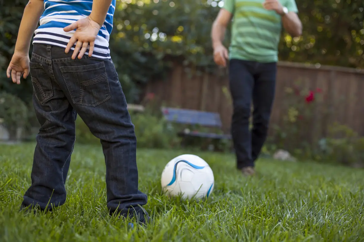 Family playing soccer on a warm-season grass lawn in a Charlotte backyard