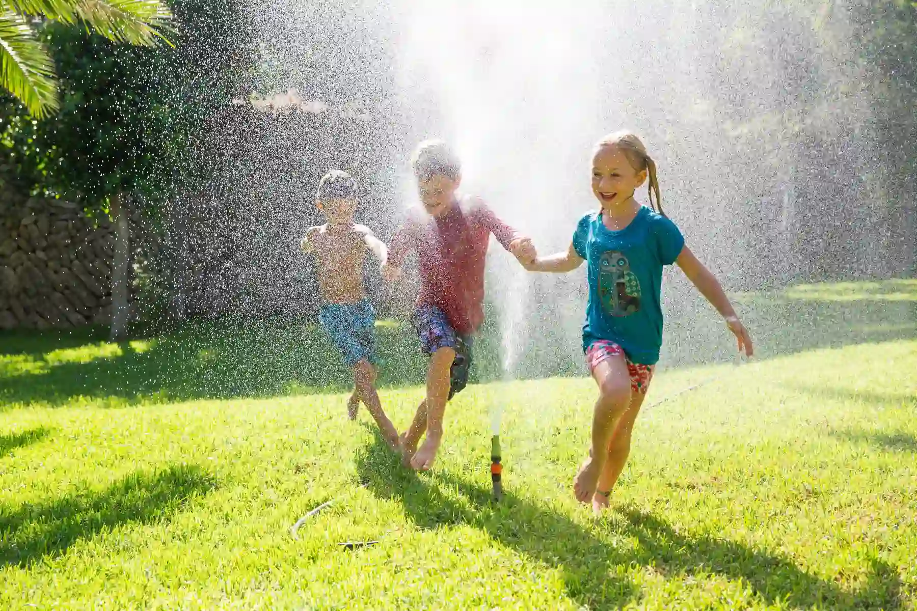 Kids running through a lawn sprinkler on a healthy green lawn in Charlotte